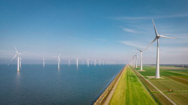 Yel değirmeni parkı Batı Hollanda, rüzgâr değirmeni türbini okyanusta mavi gökyüzü, yeşil enerji
