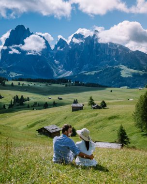 couple men and woman on vacation in the Dolomites Italy,Alpe di Siusi - Seiser Alm with Sassolungo - Langkofel mountain group in background at sunset. Yellow spring flowers and wooden chalets in clipart