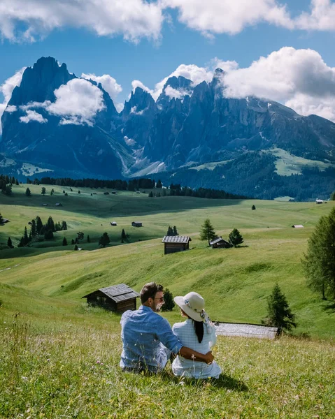 Couple men and woman on vacation in the Dolomites Italy,Alpe di Siusi - Seiser Alm with Sassolungo - Langkofel mountain group in background at sunset. Yellow spring flowers and wooden chalets in — Stock Photo, Image