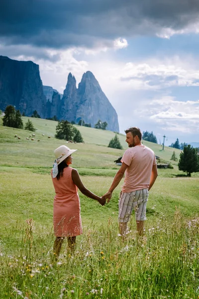 Paar im Urlaub in den Dolomiten Italien, Seiser Alm mit Langkofel-Langkofelgruppe im Hintergrund bei Sonnenuntergang. Gelbe Frühlingsblumen und Holzchalets in — Stockfoto