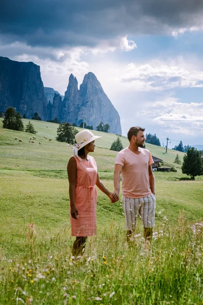 Paar im Urlaub in den Dolomiten Italien, Seiser Alm mit Langkofel-Langkofelgruppe im Hintergrund bei Sonnenuntergang. Gelbe Frühlingsblumen und Holzchalets in — Stockfoto