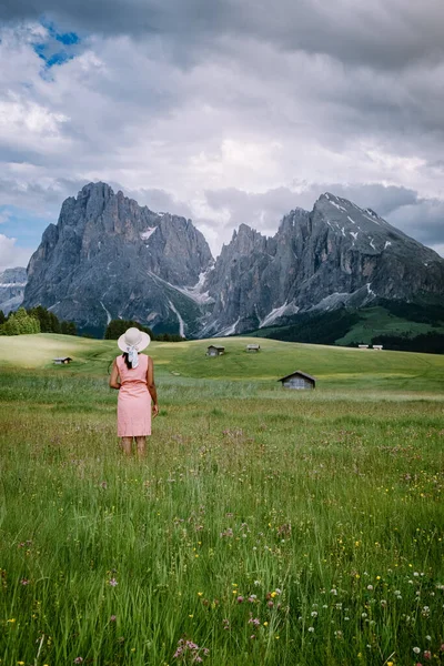 Женщина на отдыхе в Доломитовых Альпах Италии, Альпе ди Siusi - Сейзер Альм с Sassolungo - Langkofel горной группы на заднем плане на закате. Желтые весенние цветы и деревянные шале в Доломитах, Трентино — стоковое фото