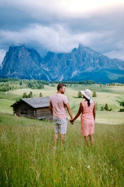 Dolomitler İtalya 'sında tatil yapan çift, Alpe di Siusi - Seiser Alm ve Sassolungo - Langkofel dağ grubu gün batımında arka planda. Sarı bahar çiçekleri ve ahşap kadehler