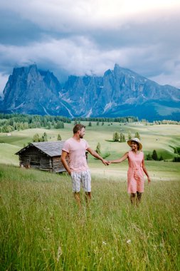 Dolomitler İtalya 'sında tatil yapan çift, Alpe di Siusi - Seiser Alm ve Sassolungo - Langkofel dağ grubu gün batımında arka planda. Sarı bahar çiçekleri ve ahşap kadehler