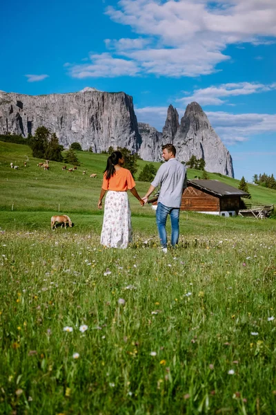 Paar mannen en vrouwen op vakantie in de Dolomieten Italië, Alpe di Siusi - Seiser Alm met Sassolungo - Langkofel berggroep op de achtergrond bij zonsondergang. Gele lentebloemen en houten chalets in — Stockfoto