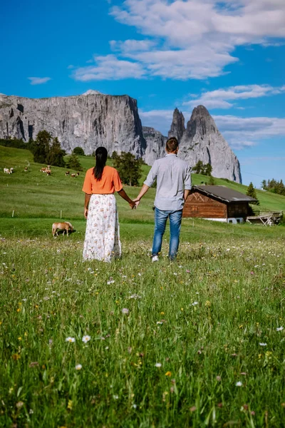 ドロミテでの休暇中のカップルの男性と女性イタリア、アルプ・ディ・シウシ-サッソルンゴとセイザー・アルム-日没時に背景にランコフェル山のグループ。黄色の春の花や木製のシャレーで — ストック写真