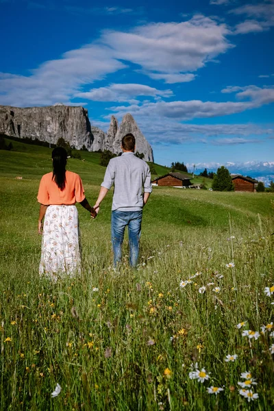 Paar im Urlaub in den Dolomiten Italien, Seiser Alm mit Langkofel-Langkofelgruppe im Hintergrund bei Sonnenuntergang. Gelbe Frühlingsblumen und Holzchalets in — Stockfoto