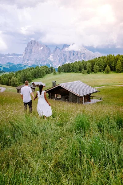 日落时分，意大利多洛美人度假时，Alpe di Siusi-Seiser Alm与Sassolungo-Langkofel山区的一组男子和女子作为背景。黄色的春花和木制的小木屋 — 图库照片