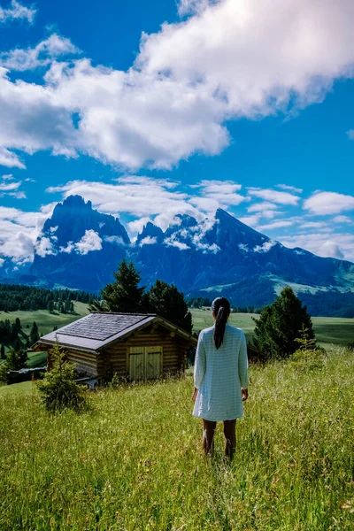 Donna in vacanza nelle Dolomiti Italia, Alpe di Siusi - Alpe di Siusi con Sassolungo - Gruppo montuoso Langkofel sullo sfondo al tramonto. Fiori gialli primaverili e chalet in legno nelle Dolomiti, Trentino — Foto Stock