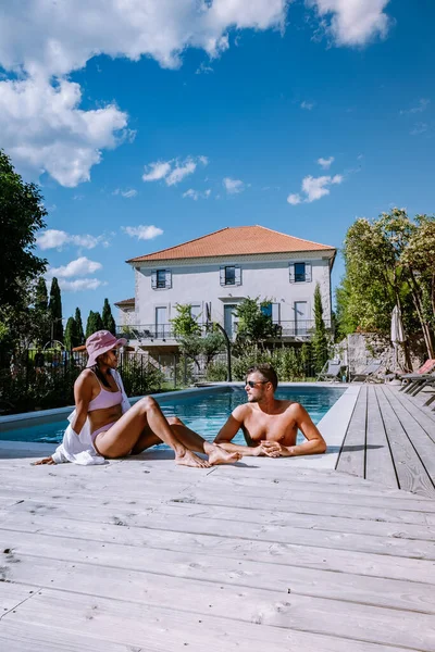 French vacation home with wooden deck and swimming pool in the Ardeche France. Couple relaxing by the pool with wooden deck during luxury vacation at an holiday home in South of France