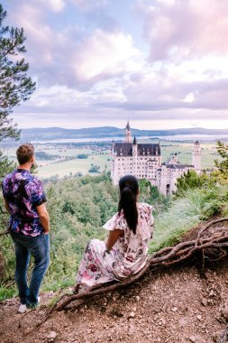 couple men and woman visit Neuschwanstein Castle. Beautiful view of world-famous Neuschwanstein Castle, the nineteenth-century Romanesque Revival palace built for King Ludwig II on a rugged cliff near clipart
