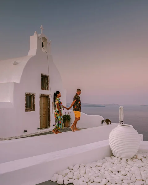 Santorini Grécia, jovem casal em férias de luxo na Ilha de Santorini assistindo ao nascer do sol pela igreja cúpula azul e aldeia caiada de branco de Oia Santorini Grécia durante o nascer do sol — Fotografia de Stock