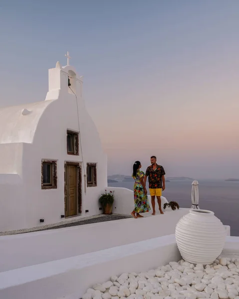 Santorini Grecja, młoda para na luksusowych wakacjach na wyspie Santorini oglądając wschód słońca przy błękitnej kopule kościoła i bielonej miejscowości Oia Santorini Grecja podczas wschodu słońca — Zdjęcie stockowe