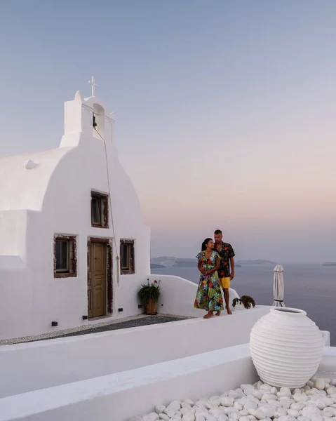 Santorini Grécia, jovem casal em férias de luxo na Ilha de Santorini assistindo ao nascer do sol pela igreja cúpula azul e aldeia caiada de branco de Oia Santorini Grécia durante o nascer do sol — Fotografia de Stock