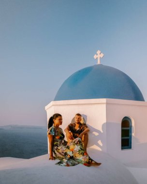 Santorini Yunanistan, genç çift güneş doğarken mavi kubbe kilisesi ve beyazlatılmış Oia Santorini köyünün gündoğumunu izlemek için Santorini Adası 'nda lüks bir tatile çıktılar.
