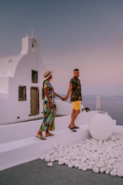 Santorini Yunanistan, Santorini Adası 'nda lüks tatilde olan genç bir çift, güneş doğarken mavi kubbe kilisesi ve beyazlatılmış Oia Santorini köyünün doğuşunu izliyor.