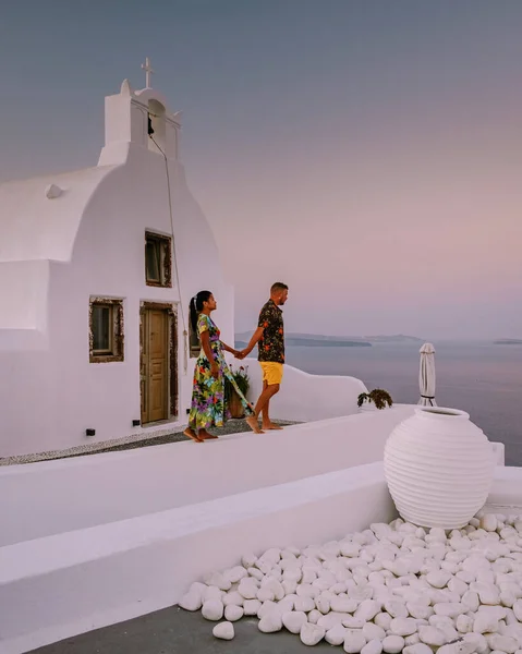 Santorini Greece, young couple on luxury vacation at the Island of Santorini watching sunrise by the blue dome church and whitewashed village of Oia Santorini Greece during sunrise — Stock Photo, Image