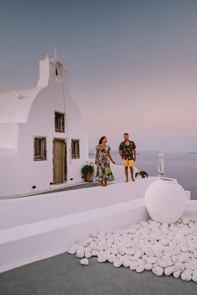 Santorini Greece, young couple on luxury vacation at the Island of Santorini watching sunrise by the blue dome church and whitewashed village of Oia Santorini Greece during sunrise — Stock Photo, Image