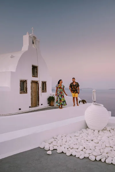 Santorini Grécia, jovem casal em férias de luxo na Ilha de Santorini assistindo ao nascer do sol pela igreja cúpula azul e aldeia caiada de branco de Oia Santorini Grécia durante o nascer do sol — Fotografia de Stock