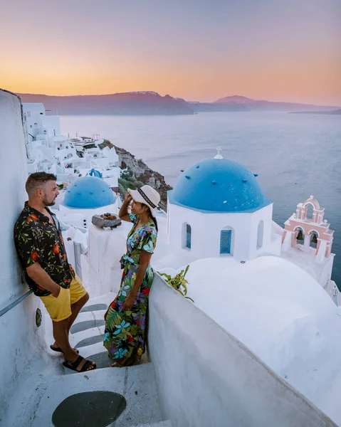 Santorini Görögország, fiatal pár luxus nyaralás a sziget Santorini nézi napkelte a kék kupola templom és fehérre meszelt falu Oia Santorini Görögország napkeltekor, férfiak és nők a — Stock Fotó