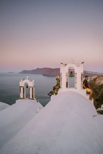 Santorini Grecia, pareja joven en vacaciones de lujo en la isla de Santorini viendo el amanecer por la iglesia de cúpula azul y el pueblo encalado de Oia Santorini Grecia durante el amanecer, hombres y mujeres en — Foto de Stock