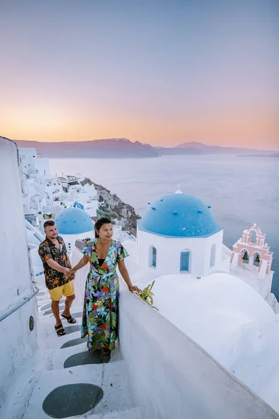 Santorini Grecia, pareja joven en vacaciones de lujo en la isla de Santorini viendo el amanecer por la iglesia de cúpula azul y el pueblo encalado de Oia Santorini Grecia durante el amanecer, hombres y mujeres en — Foto de Stock