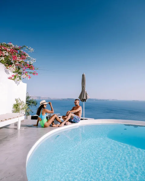 Santorini Grecia, pareja joven en vacaciones de lujo en la isla de Santorini viendo el amanecer por la iglesia de cúpula azul y el pueblo encalado de Oia Santorini Grecia durante el amanecer, hombres y mujeres en —  Fotos de Stock