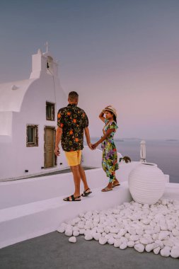 Santorini Yunanistan, Santorini Adası 'nda lüks tatilde olan genç bir çift, güneş doğarken mavi kubbe kilisesi ve beyazlatılmış Oia Santorini köyünün doğuşunu izliyor.