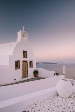 Yunanistan 'ın Santorini Adası' nda gün batımı, güzel, bembeyaz bir köy olan Oia 'da gün batımında kilise ve yel değirmeni.