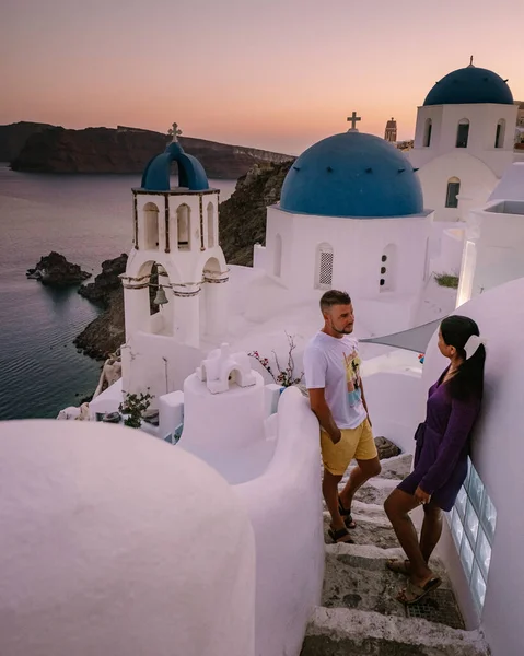 Santorini Grécia, jovem casal em férias de luxo na Ilha de Santorini assistindo ao nascer do sol pela igreja cúpula azul e aldeia caiada de branco de Oia Santorini Grécia durante o nascer do sol — Fotografia de Stock