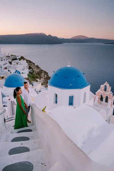 圣托里尼希腊，一对年轻夫妇在圣托里尼岛上观看着蓝色穹顶教堂的日出，日出时在粉刷过的希腊奥亚圣托里尼村，男男女女都在 — 图库照片
