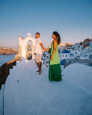 Santorini Yunanistan, genç çift güneş doğarken mavi kubbe kilisesi ve beyazlatılmış Oia Santorini köyünün gündoğumunu izlemek için Santorini Adası 'nda lüks bir tatile çıktılar.