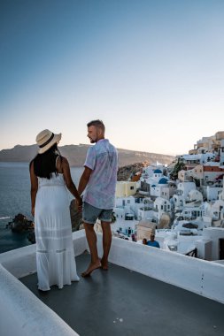 Santorini Yunanistan, genç çift güneş doğarken mavi kubbe kilisesi ve beyazlatılmış Oia Santorini köyünün gündoğumunu izlemek için Santorini Adası 'nda lüks bir tatile çıktılar.