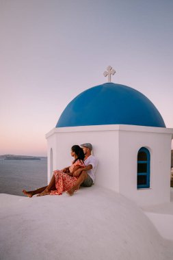 Santorini Yunanistan, genç çift güneş doğarken mavi kubbe kilisesi ve beyazlatılmış Oia Santorini köyünün gündoğumunu izlemek için Santorini Adası 'nda lüks bir tatile çıktılar.