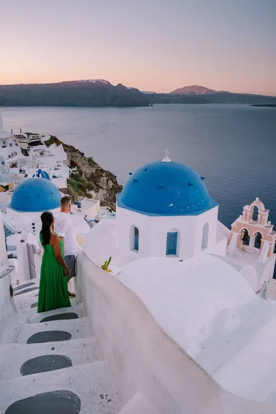 Santorini Grécia, jovem casal em férias de luxo na Ilha de Santorini assistindo ao nascer do sol pela igreja cúpula azul e aldeia caiada de branco de Oia Santorini Grécia durante o nascer do sol, homens e mulheres em — Fotografia de Stock