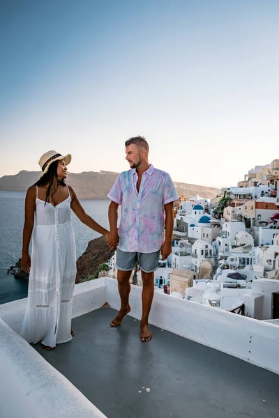 Santorini Greece, young couple on luxury vacation at the Island of Santorini watching sunrise by the blue dome church and whitewashed village of Oia Santorini Greece during sunrise, men and woman on — Stock Photo, Image