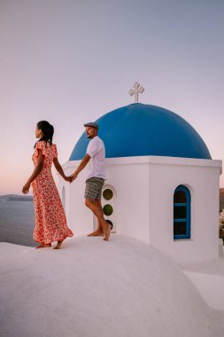 Santorini Yunanistan, genç çift güneş doğarken mavi kubbe kilisesi ve beyazlatılmış Oia Santorini köyünün gündoğumunu izlemek için Santorini Adası 'nda lüks bir tatile çıktılar.