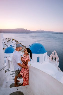 Santorini Yunanistan, genç çift güneş doğarken mavi kubbe kilisesi ve beyazlatılmış Oia Santorini köyünün gündoğumunu izlemek için Santorini Adası 'nda lüks bir tatile çıktılar.