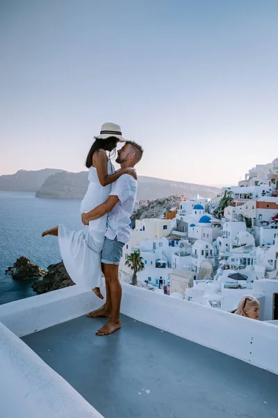 Santorini Greece, young couple on luxury vacation at the Island of Santorini watching sunrise by the blue dome church and whitewashed village of Oia Santorini Greece during sunrise, men and woman on — Stock Photo, Image