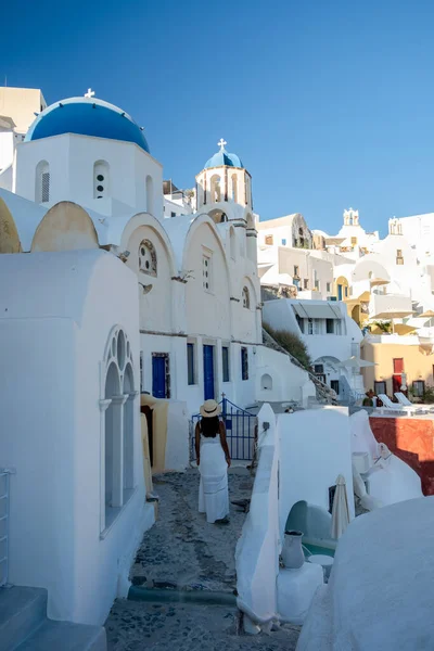 Santorini Grecia, pareja joven en vacaciones de lujo en la isla de Santorini viendo el amanecer por la iglesia de cúpula azul y el pueblo encalado de Oia Santorini Grecia durante el amanecer, hombres y mujeres en — Foto de Stock