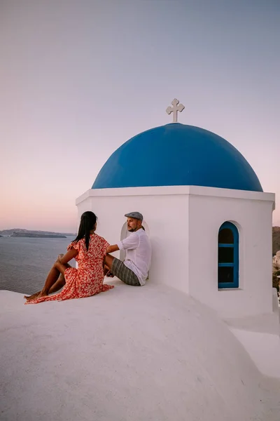 Santorini Grecja, młoda para na luksusowych wakacjach na wyspie Santorini oglądać wschód słońca przy błękitnej kopule kościoła i bielone wioski Oia Santorini Grecja podczas wschodu słońca, mężczyźni i kobiety na — Zdjęcie stockowe