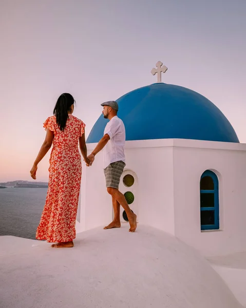 Santorini Greece, young couple on luxury vacation at the Island of Santorini watching sunrise by the blue dome church and whitewashed village of Oia Santorini Greece during sunrise, men and woman on — Stock Photo, Image