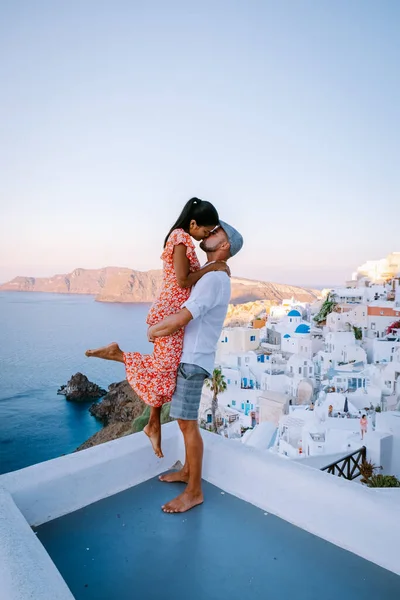 Santorini Greece, young couple on luxury vacation at the Island of Santorini watching sunrise by the blue dome church and whitewashed village of Oia Santorini Greece during sunrise, men and woman on — Stock Photo, Image