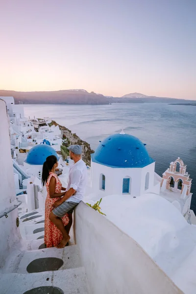 Santorini Greece, young couple on luxury vacation at the Island of Santorini watching sunrise by the blue dome church and whitewashed village of Oia Santorini Greece during sunrise, men and woman on — Stock Photo, Image