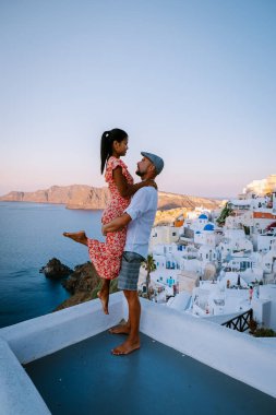 Santorini Yunanistan, genç çift güneş doğarken mavi kubbe kilisesi ve beyazlatılmış Oia Santorini köyünün gündoğumunu izlemek için Santorini Adası 'nda lüks bir tatile çıktılar.