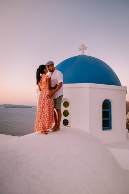 Santorini Yunanistan, genç çift güneş doğarken mavi kubbe kilisesi ve beyazlatılmış Oia Santorini köyünün gündoğumunu izlemek için Santorini Adası 'nda lüks bir tatile çıktılar.
