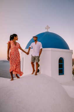Santorini Yunanistan, genç çift güneş doğarken mavi kubbe kilisesi ve beyazlatılmış Oia Santorini köyünün gündoğumunu izlemek için Santorini Adası 'nda lüks bir tatile çıktılar.