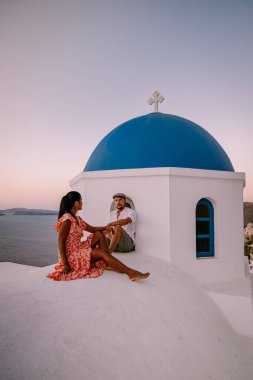 Santorini Yunanistan, genç çift güneş doğarken mavi kubbe kilisesi ve beyazlatılmış Oia Santorini köyünün gündoğumunu izlemek için Santorini Adası 'nda lüks bir tatile çıktılar.