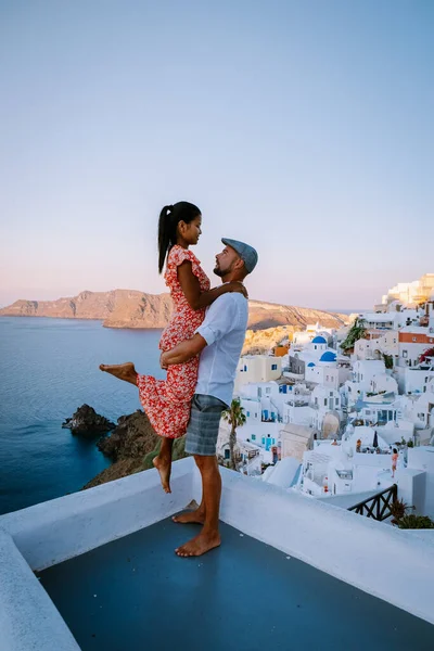 Santorini Grecia, giovane coppia in vacanza di lusso all'isola di Santorini guardando l'alba dalla chiesa cupola blu e villaggio imbiancato di Oia Santorini Grecia durante l'alba, uomini e donne su — Foto Stock