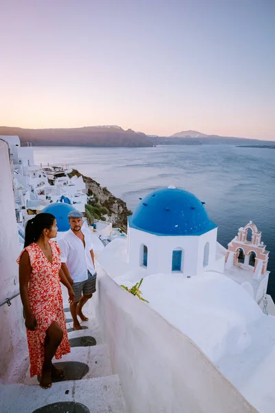 Santorini Greece, young couple on luxury vacation at the Island of Santorini watching sunrise by the blue dome church and whitewashed village of Oia Santorini Greece during sunrise, men and woman on — Stock Photo, Image